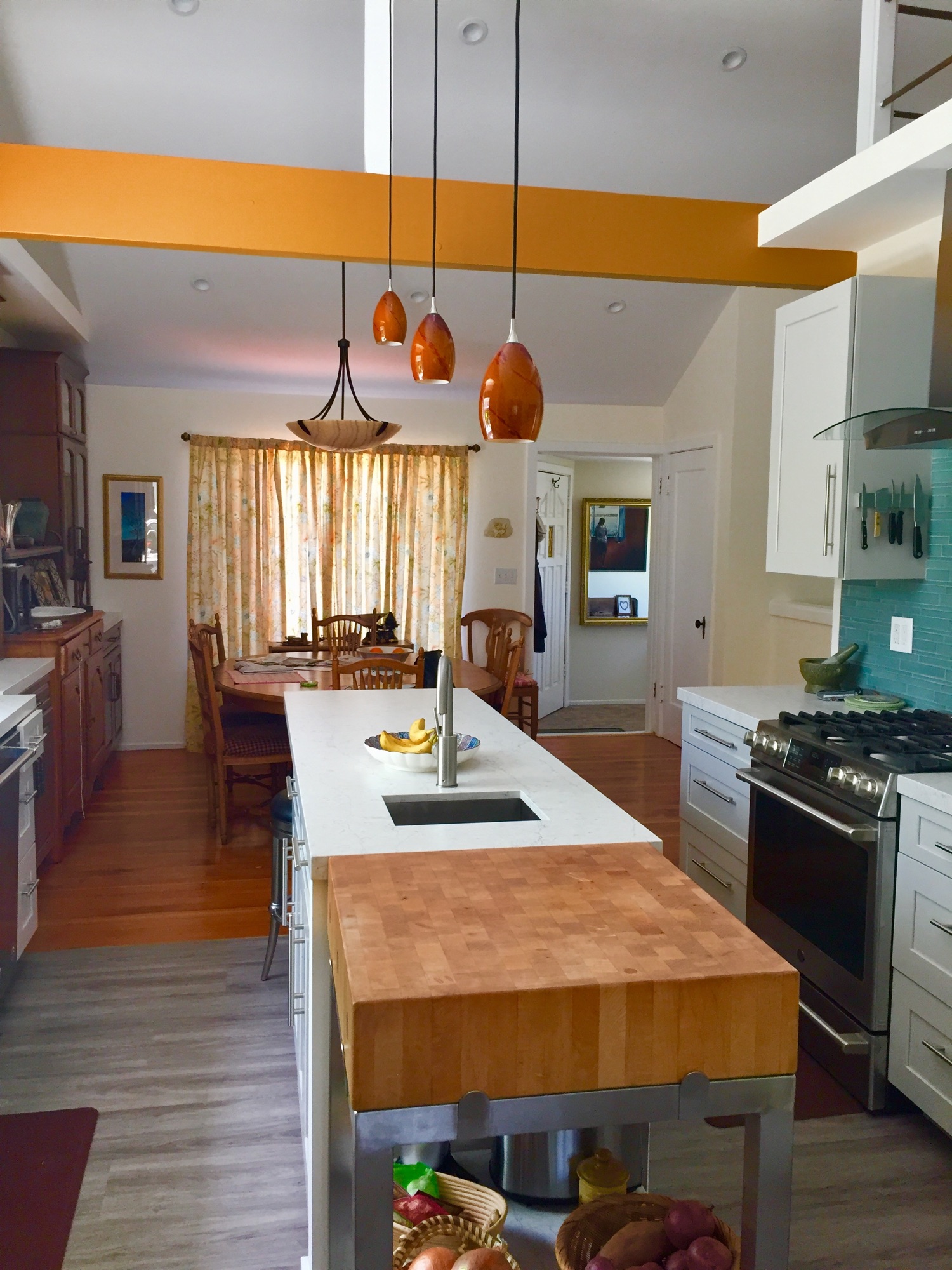 Kitchen with white cabinets, a marble island and wood butcher block, a turquoise tile backsplash, and a dining table beyond.